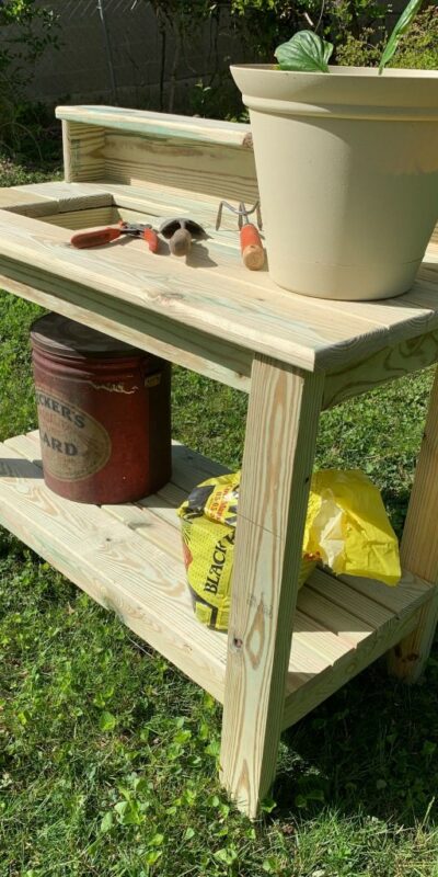 Potting table with potted plant, potting supplies, and garden tools.